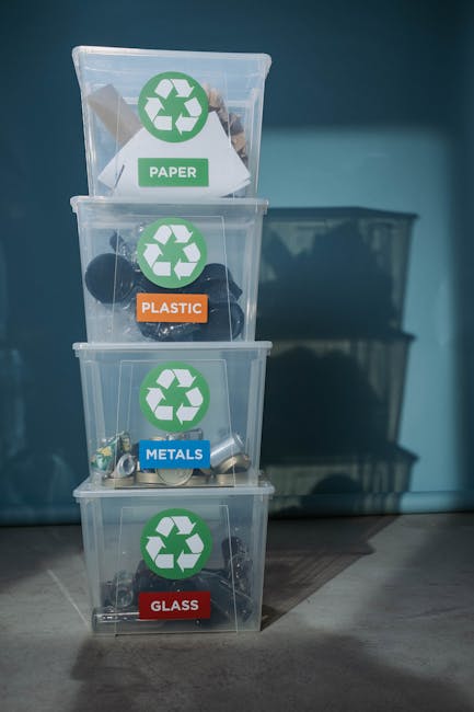 A person's hand holding a clear glass bottle over a white plastic container filled with several other empty glass bottles and jars, some of which are brown or green. The jars are of various sizes and